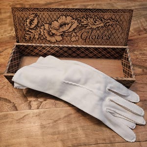 May include: A pair of white gloves in a wooden box with a floral design and the word "Gloves" engraved on the lid.