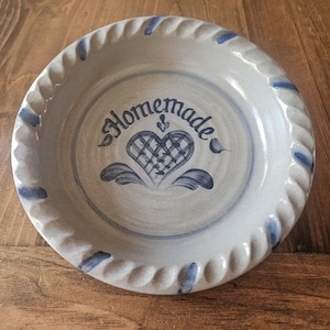 May include: A blue and white ceramic pie plate with a rope design around the edge. The plate has a blue heart with a checkered pattern and the word "Homemade" written in blue cursive.