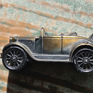May include: A vintage-style miniature car with a bronze and black finish. The classic roadster features black spoked wheels, a detailed grill, and a convertible top. The model car is a decorative item.