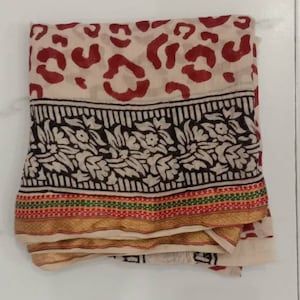 Puede incluir: Una tela beige doblada con un diseño de estampado de leopardo rojo y blanco. La tela tiene un borde floral blanco y negro y un ribete dorado, rojo, verde y blanco.