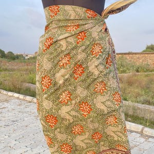 May include: A green sarong with a floral and paisley pattern, wrapped around a mannequin. The sarong features red and orange flowers, cream paisley designs, and a cream border. The fabric is tied at the waist.