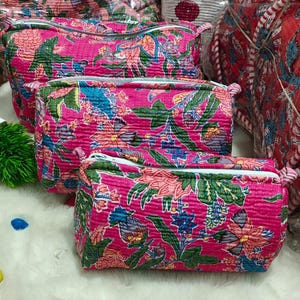 May include: Three rectangular quilted pouches in a vibrant hot pink fabric featuring a multi-coloured floral print with green leaves and blue accents. Each pouch has a white zip closure along the top edge and a soft, textured quilted finish.