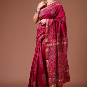 May include: A magenta handblock Maheshwari saree with intricate patterns in red, blue, and gold. The saree features detailed borders and a decorative design. The image includes the text "HANDBLOCK MAHESHWARI SAREE".