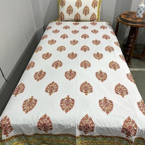 May include: A white bed sheet and matching pillowcase featuring a repeating orange and yellow floral tree pattern. The bedding set includes a decorative border with yellow and green geometric stripes along the bottom edge of the sheet.