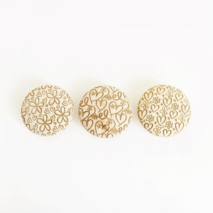 May include: Three round wooden buttons with a gold-coloured pattern of hearts and flowers.