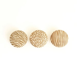 Peut inclure: Trois sous-verres ronds en bois avec différents motifs d'imprimés animaliers. Les sous-verres présentent un imprimé zèbre, un imprimé léopard et un motif de grain de bois.