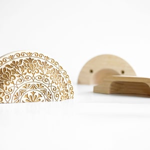 May include: Light wood cabinet pulls with a floral design. The semi-circular pulls feature carved patterns. The image shows three pieces: a handle and mounting hardware. The pulls are made of light-coloured wood.