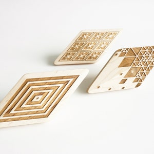 Peut inclure: Trois objets décoratifs en bois en forme de losange avec des motifs géométriques complexes. L'un présente des carrés concentriques, un autre des motifs floraux et le troisième un motif triangulaire. Les objets sont marron clair et beiges.