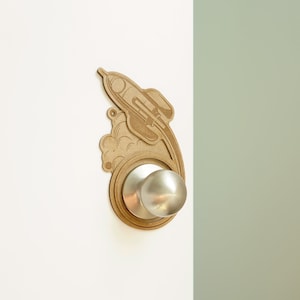 May include: A silver door knob with a rocket ship design on a brown wooden plaque.