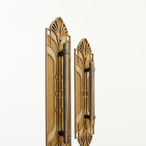 Pode incluir: Duas maçanetas de porta decorativas com um design Art Deco. As maçanetas são feitas de madeira e metal e têm um acabamento castanho.