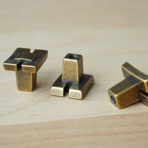 Könnte beinhalten: Drei antike goldene Schrankknöpfe mit geometrischem Design. Die Knöpfe haben eine quadratische Basis und eine rechteckige Oberseite mit einem Ausschnitt in der Mitte.