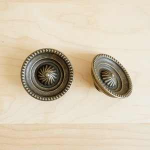 May include: Two antique brass cabinet knobs with a decorative, raised, circular design in the centre.