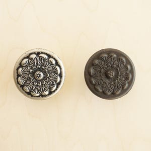 May include: Two round, decorative cabinet knobs with a floral design. One knob is silver and the other is dark brown.
