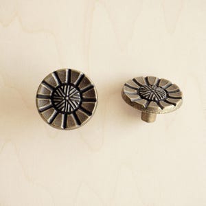 May include: Two antique brass cabinet knobs with a circular design featuring a raised, intricate, sunburst pattern. The knobs have a slightly aged finish.