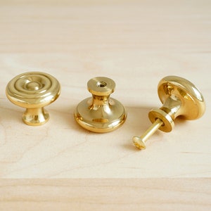 Peut inclure: Trois boutons de porte en or avec un design rond légèrement surélevé. Les boutons ont une finition lisse et polie.