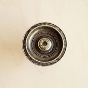 May include: A round, brass cabinet knob with a decorative, concentric circle design.