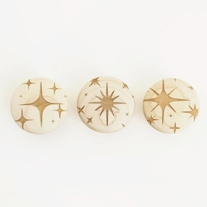 Op de afbeelding: Drie houten kastknoppen met sterrenpatronen. De knoppen zijn van lichtgekleurd hout met geëtste sterpatronen in een donkerdere bruine kleur. De sterrenpatronen variëren in grootte en stijl, wat een decoratief accent creëert.