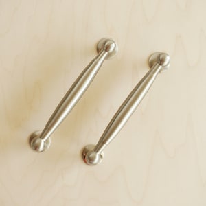 Op de afbeelding: Twee zilveren kastdeurgrepen met afgeronde uiteinden.