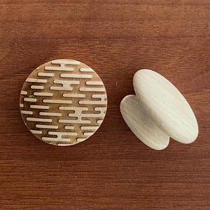 Könnte beinhalten: Ein Set aus Holzhandwerk auf einer braunen Oberfläche. Das Set enthält ein rundes, hellbraunes Stück mit einem sich wiederholenden Muster aus horizontalen Linien und zwei oval geformte, hellfarbige Holzstücke.