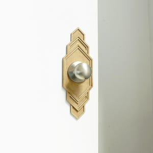 May include: A silver door knob with a decorative wooden frame. The frame is made of multiple layers of wood, creating a geometric pattern.