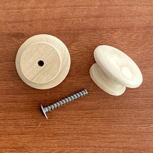 May include: A set of wooden furniture hardware, comprising two round knobs, two oval knobs, and a silver screw. The knobs are light-coloured and unfinished. The screw has a flat head.