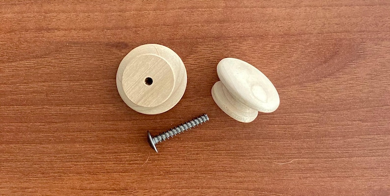 May include: A set of wooden furniture hardware, comprising two round knobs, two oval knobs, and a silver screw. The knobs are light-coloured and unfinished. The screw has a flat head.