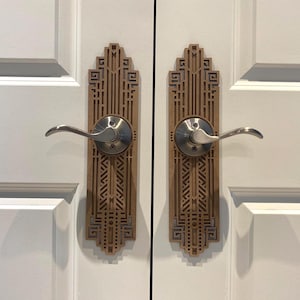 Peut inclure: Deux plaques de poignée de porte assorties présentant un motif géométrique marron découpé au laser avec des lignes verticales et des formes rectangulaires complexes. Chaque plaque est centrée autour d'une poignée en métal argenté.