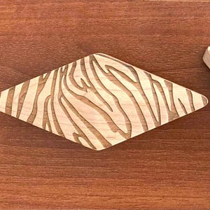 Peut inclure: Tiroirs en bois en forme de losange avec un motif de rayures zébrées. Les poignées sont en bois de couleur claire avec un motif de grain de bois plus foncé contrastant. Elles sont posées sur une surface en bois marron.