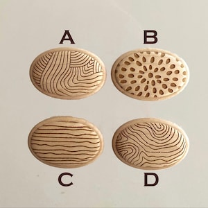 Op de afbeelding: Vier ovale houten stempels gelabeld A, B, C en D. Stempel A heeft een patroon van golvende lijnen, B een radiaal bloembladontwerp, C horizontale golvende lijnen en D een topografisch hoogtelijnenpatroon. Elke stempel heeft een lichte houtafwerking.