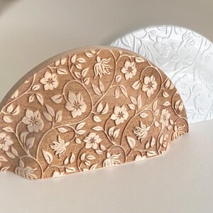 Puede incluir: Dos piezas decorativas de madera semicirculares. Una es de color marrón claro con un patrón floral tallado en la superficie. La otra es blanca con un diseño floral en relieve similar. Probablemente son para la decoración del hogar.