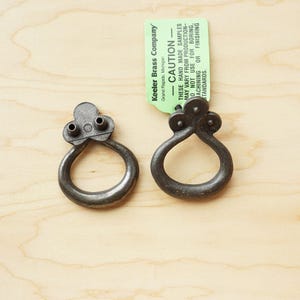 May include: Two antique-style metal drawer pulls with a ring shape and a decorative top. The pulls are a dark gray color and have a distressed finish.