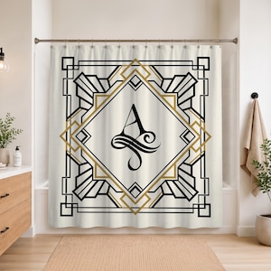 May include: A cream-colored shower curtain featuring a central black letter A monogram enclosed within a geometric frame of black and gold lines. The design includes symmetrical angular patterns and decorative flourishes surrounding the letter.