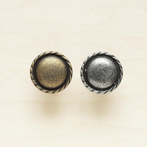 May include: Two round cabinet knobs with a rope design border. One knob is a brass finish and the other is a silver finish.