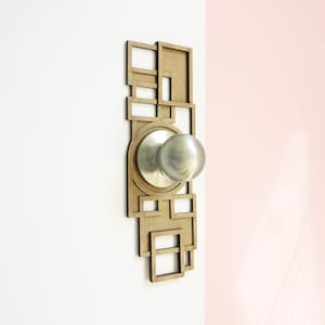 Op de afbeelding: Een zilveren deurklink met een geometrisch houten frame. Het frame is gemaakt van meerdere vierkanten en rechthoeken.