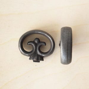 Può includere: Due tiretti per cassetti in metallo in stile antico con un design decorativo a volute. I tiretti sono di colore grigio scuro e hanno una finitura leggermente usurata.