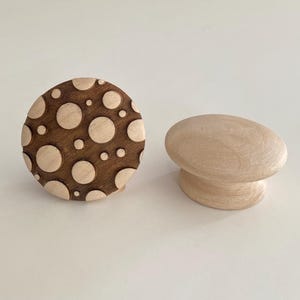 May include: Two wooden cabinet knobs. One is round with a dark brown background and light brown polka dots. The other is a light brown, oval-shaped knob with a rounded base. Both are set against a white background.