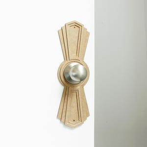 Könnte beinhalten: Ein hellbrauner, hölzerner Türknauf mit einem runden, silbernen Knauf in der Mitte. Der Knauf ist von einem dekorativen Design mit geometrischen Formen umgeben.