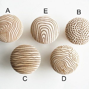 Może przedstawiać: Pięć okrągłych drewnianych gałek z różnymi grawerowanymi wzorami. Gałki są oznaczone od A do E.