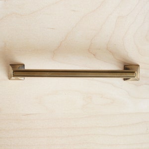 May include: A brushed gold cabinet pull with a rectangular shape and squared ends.
