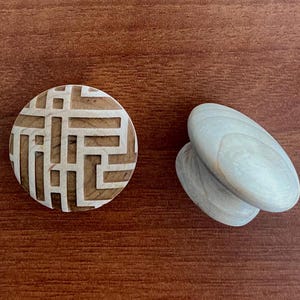 Könnte beinhalten: Ein rundes Holzobjekt mit geometrischem Design und zwei oval geformten, hellfarbigen Holzobjekten. Die Objekte befinden sich auf einer braunen Holzoberfläche. Das runde Objekt hat ein hellfarbiges geometrisches Muster.