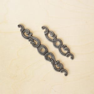 May include: Two ornate metal drawer pulls with a silver finish and intricate scrollwork designs.