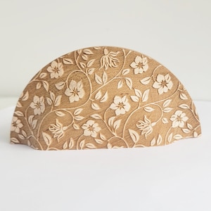 May include: A wooden napkin holder shaped like a half-circle with a floral pattern carved into the surface.