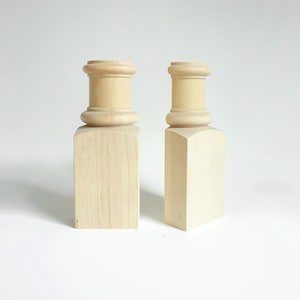 May include: Two unfinished wooden candle holders with a simple, rounded design. The holders are made of natural wood and have a smooth, polished finish.