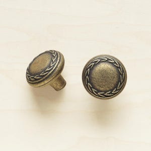 May include: Two antique brass cabinet knobs with a decorative rope design around the edge.