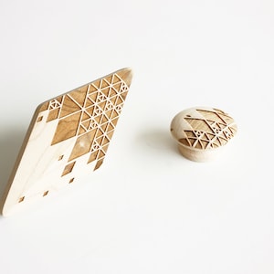 May include: Two wooden pieces with a geometric pattern carved into the surface. The larger piece is a flat, diamond-shaped piece. The smaller piece is a round knob.