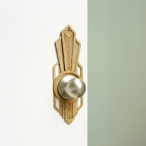 Op de afbeelding: Een houten deurknop met een Art Deco-ontwerp. De knop is gemaakt van hout en heeft een zilveren afwerking. Het ontwerp is ingewikkeld en heeft geometrische vormen.