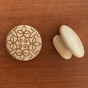 May include: A set of wooden craft items. One is a round piece with an engraved floral pattern, and two are oval-shaped. The items are light-coloured and rest on a brown wooden surface.