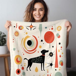 May include: A cream-colored fleece blanket featuring a black dog silhouette with white circular patterns on its body. The design includes scattered geometric shapes, including red circles, yellow rings, and black starbursts, arranged in a mid-century style.