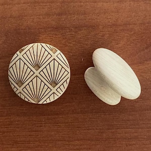 Peut inclure: Deux objets décoratifs en bois sur une surface marron. L'un est un bouton rond avec un motif géométrique en éventail. L'autre est une paire d'objets en bois de forme ovale. Les objets sont en bois de couleur claire.