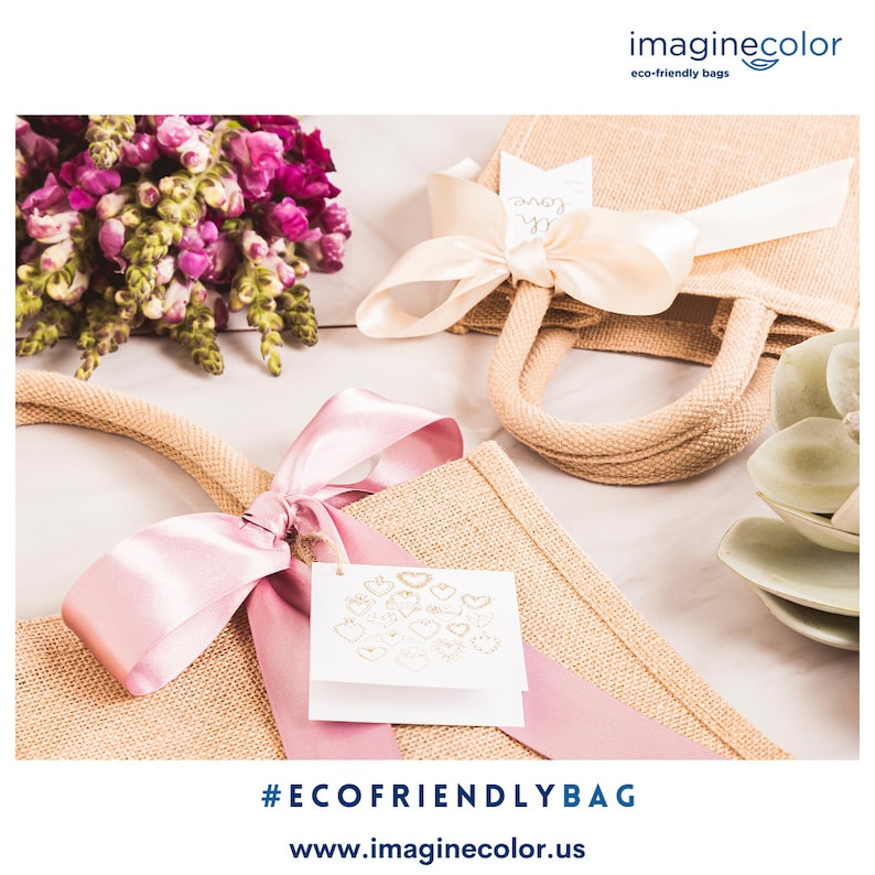 May include: Eco-friendly jute tote bags with pink satin ribbons and tags. One bag has a cream-colored bow. The bags have jute handles and are decorated with floral arrangements. The image includes the text "#ECOFRIENDLYBAG" and "www.imaginecolor.us".
